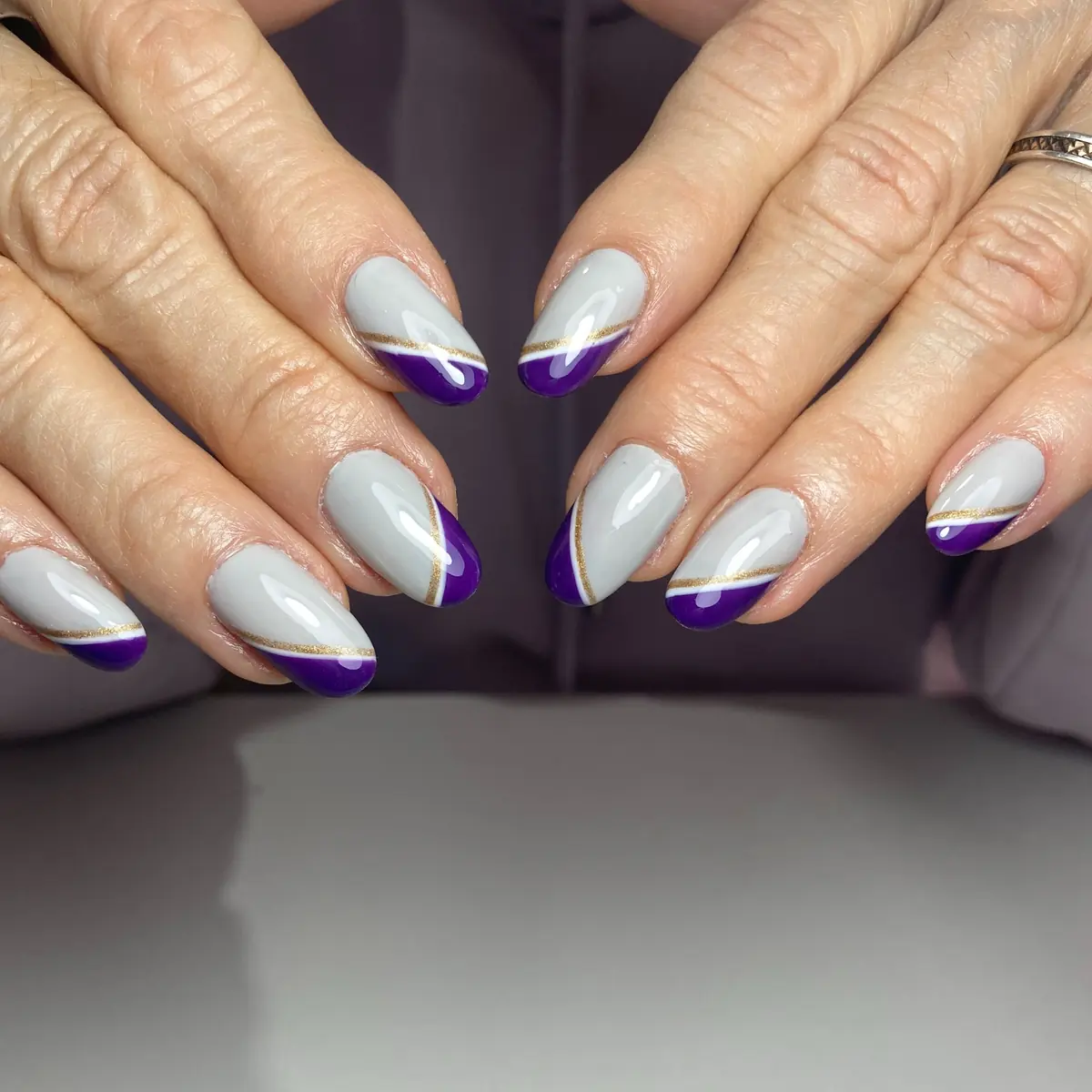 Uñas gris con punta violeta en diagonal y línea dorada
